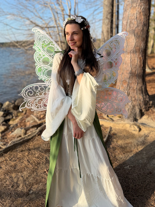 Woman in a white dress with fairy wings standing by a body of water.
