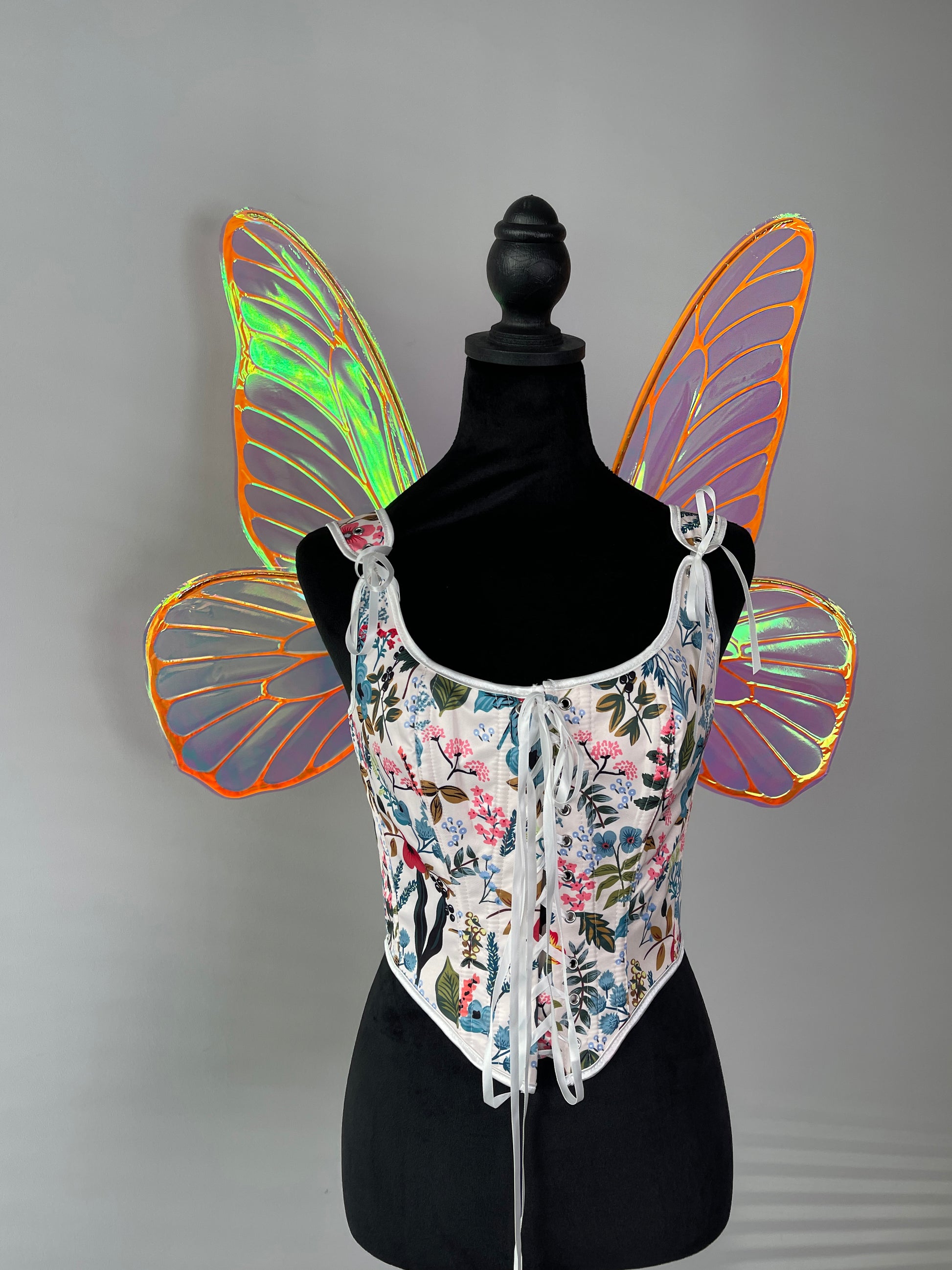 Mannequin wearing a floral corset with colorful butterfly wings on a gray background