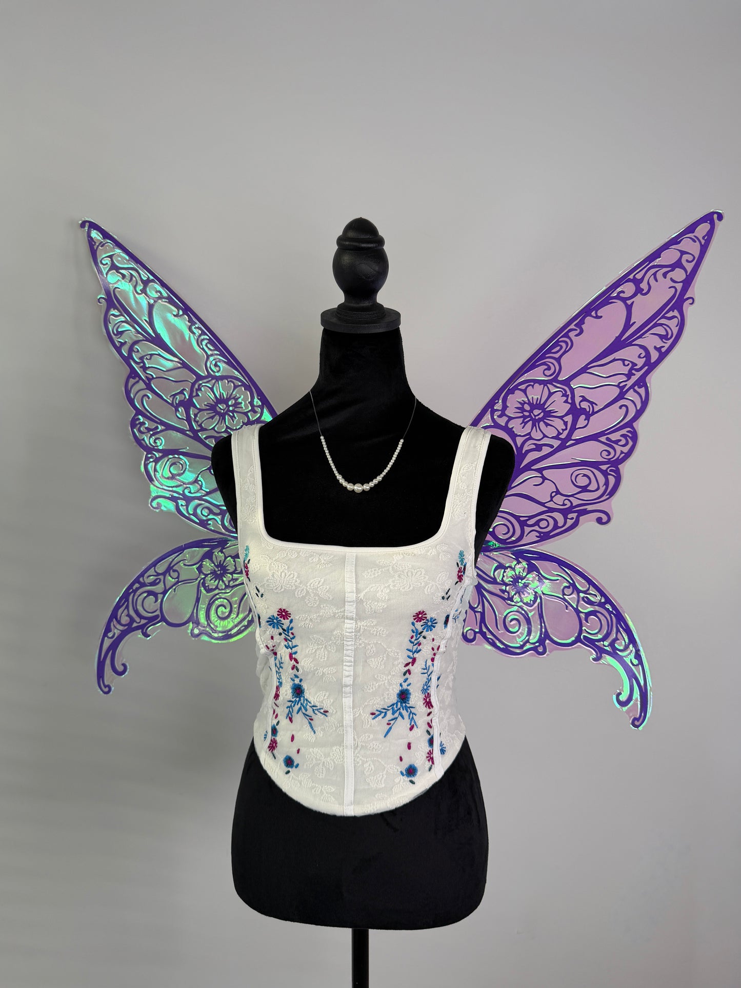 White corset with floral embroidery on a mannequin wearing purple butterfly wings.