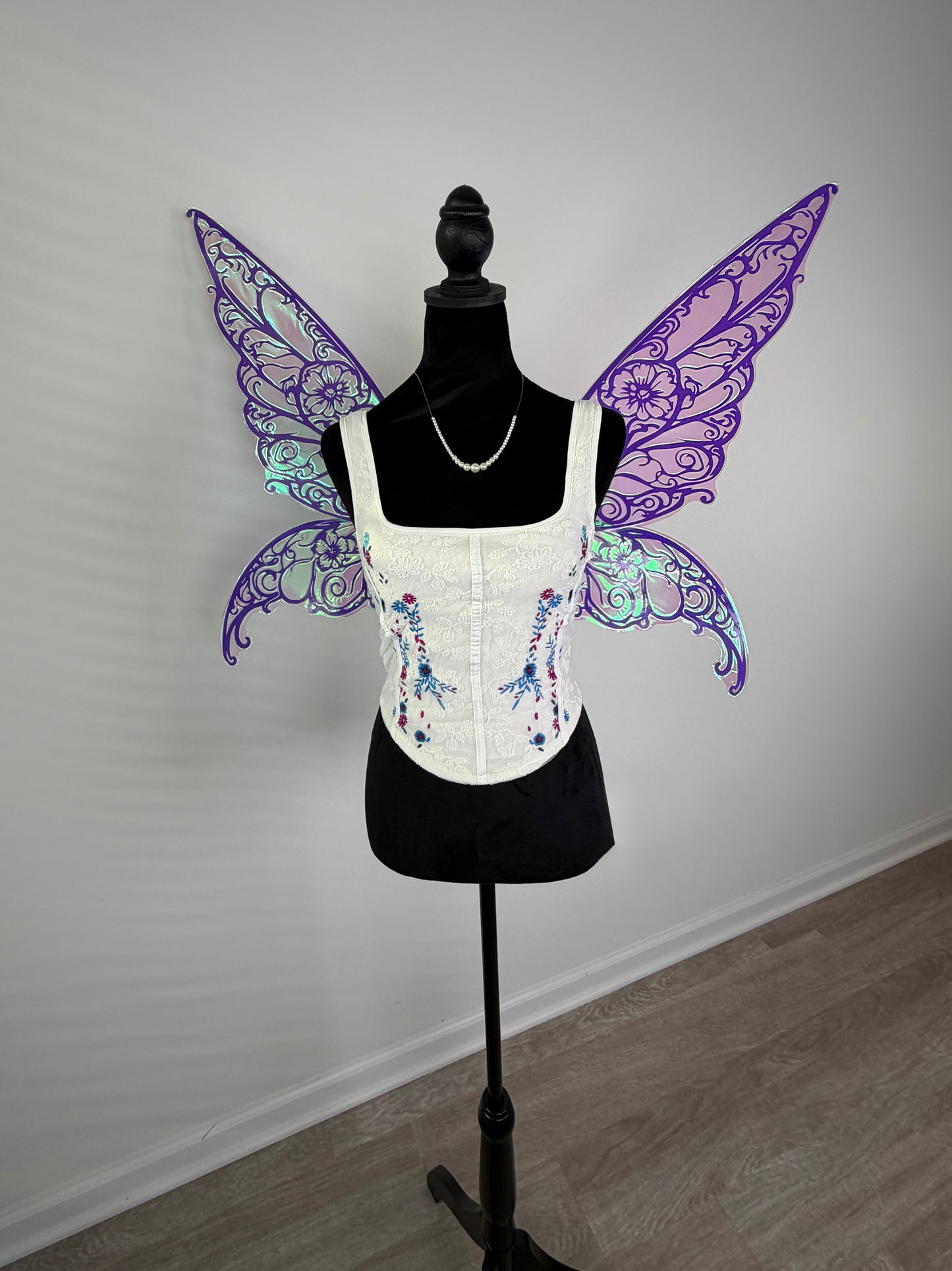 Mannequin wearing a white corset with colorful butterfly wings against a plain background