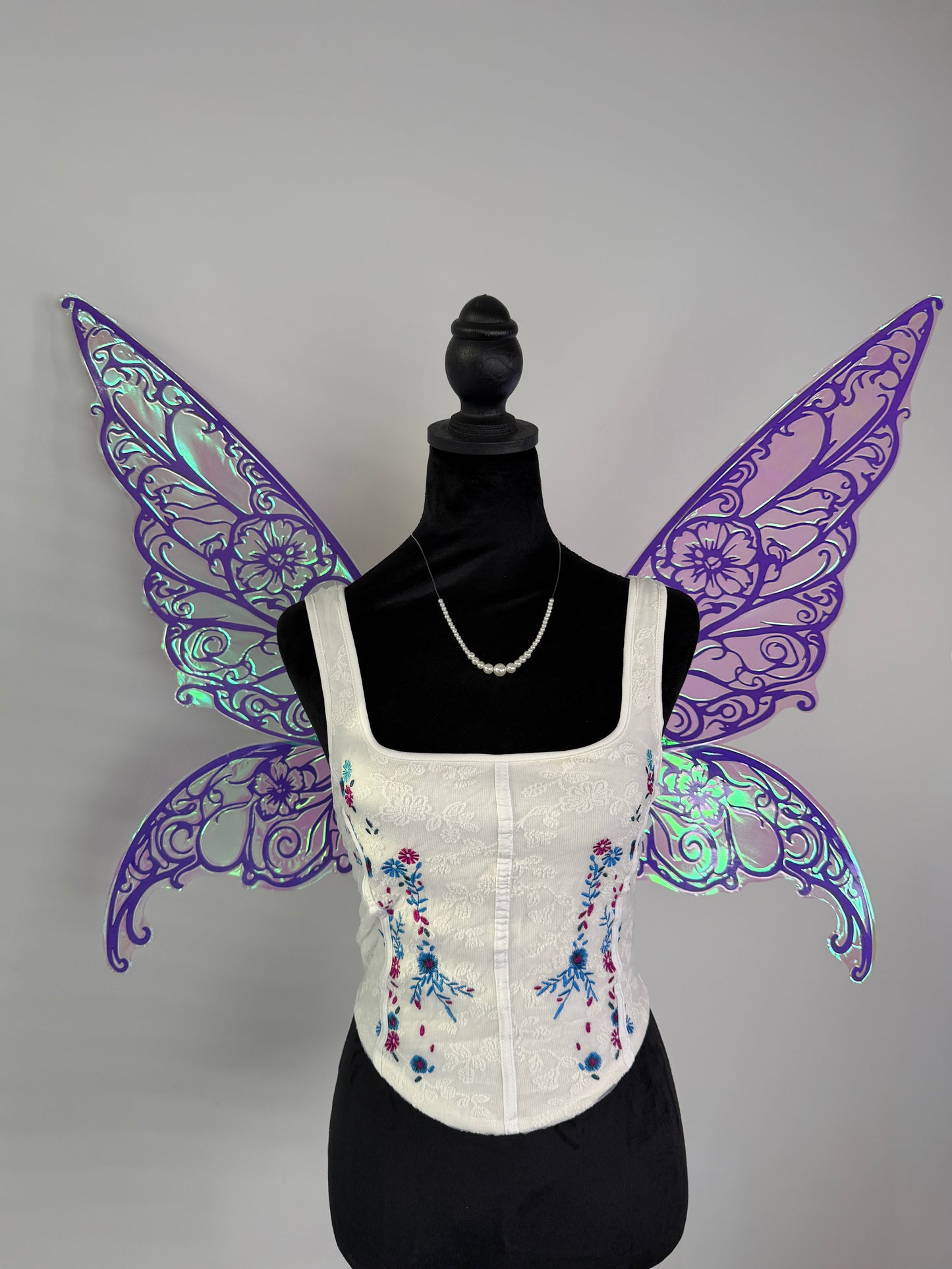 White corset with purple fairy wings on a mannequin against a gray background