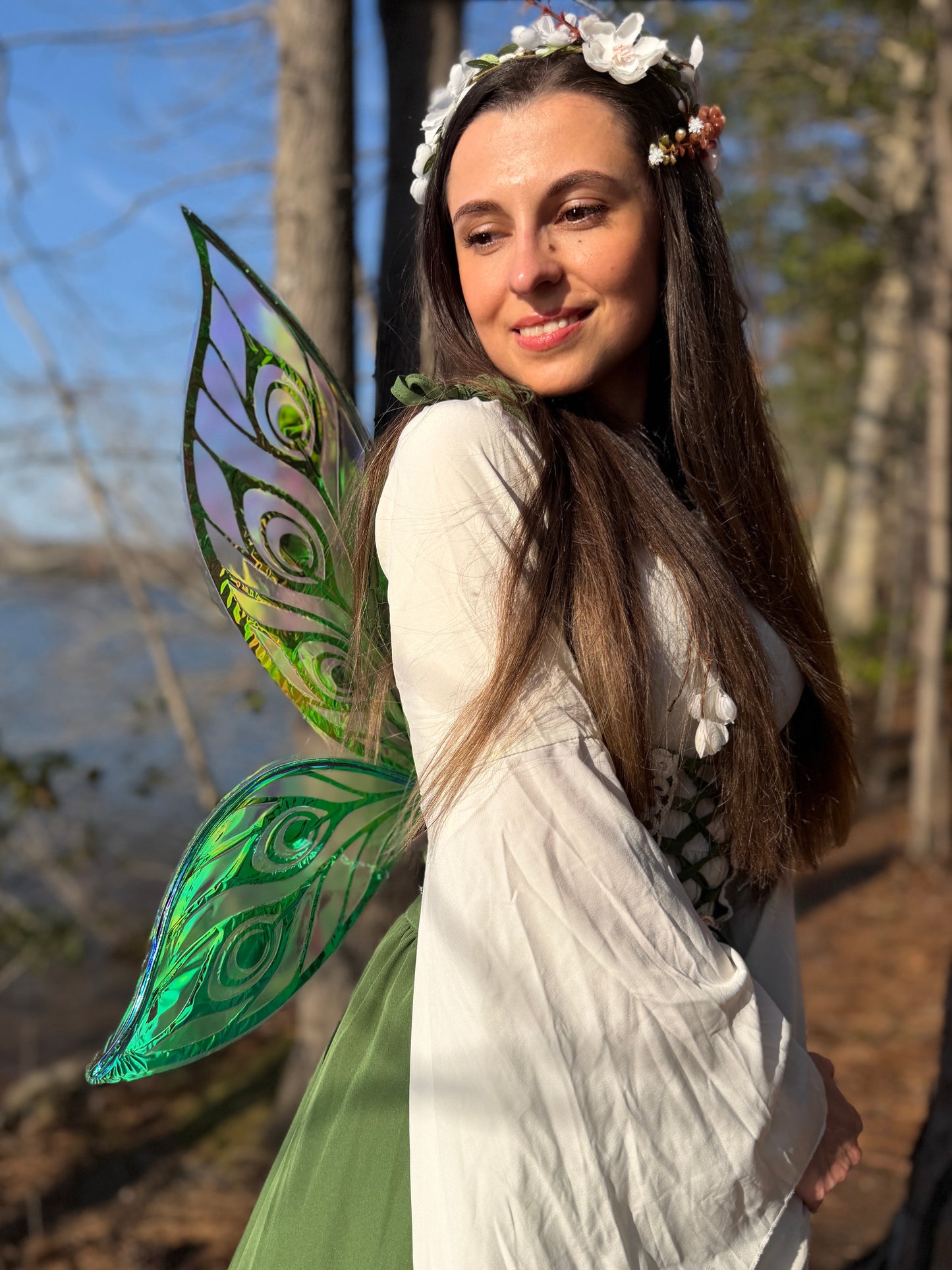 Woman with fairy wings and floral headband standing outdoors near water