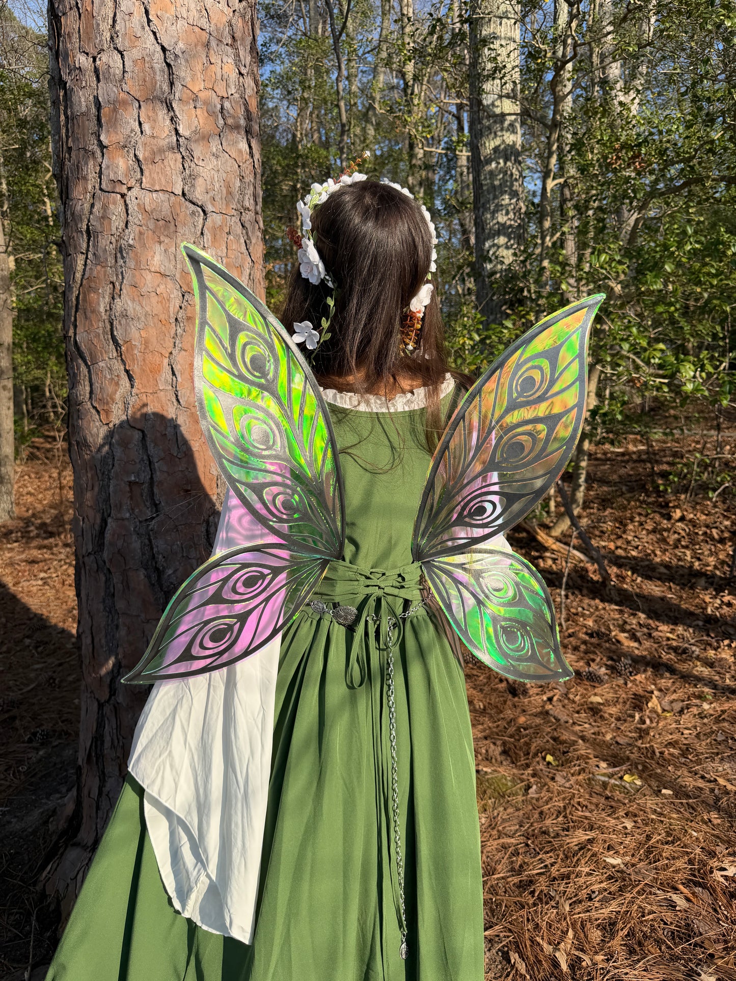 Person wearing a green dress with colorful fairy wings in a forest setting