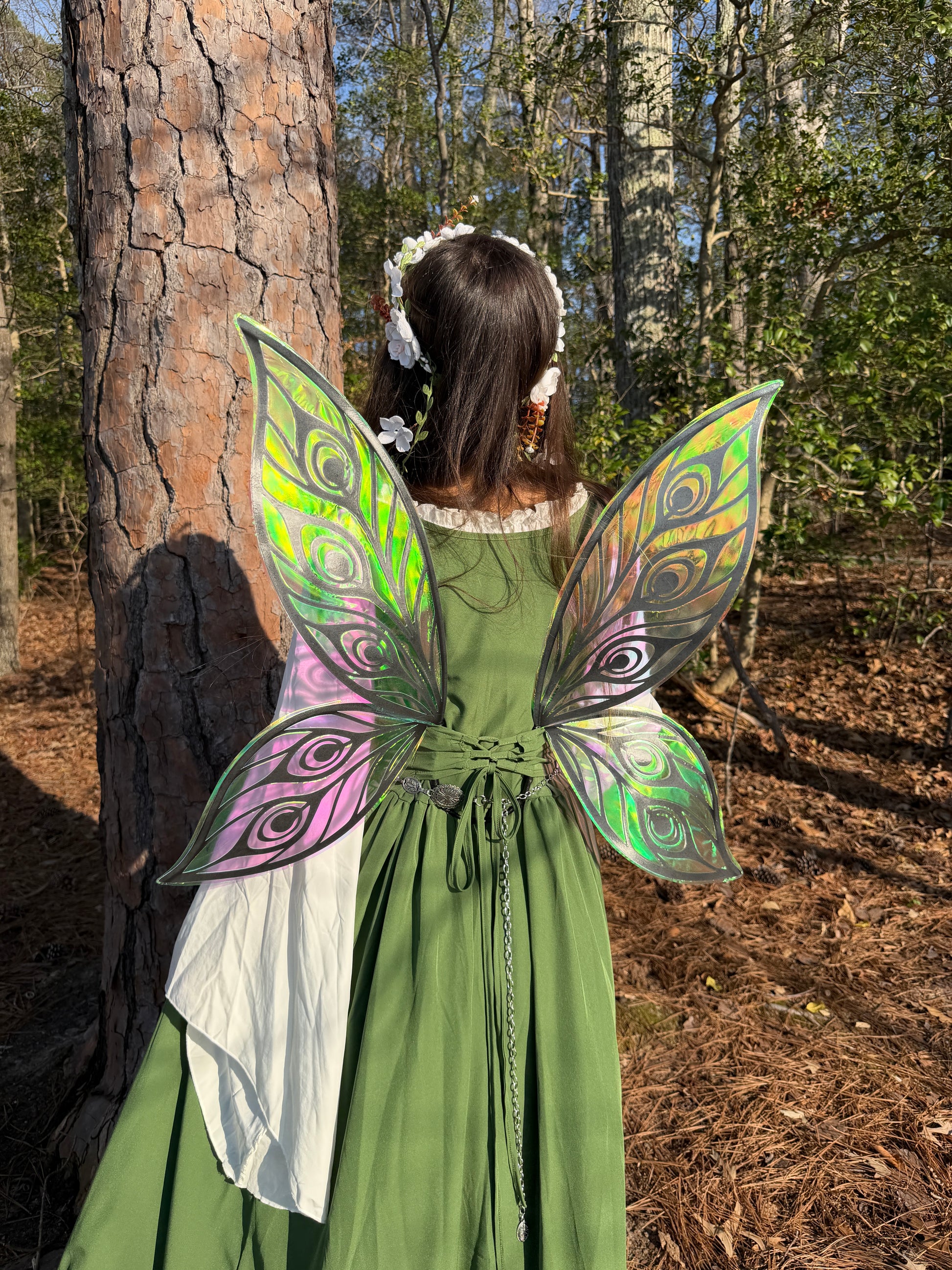 Person wearing a green dress with colorful fairy wings in a forest setting