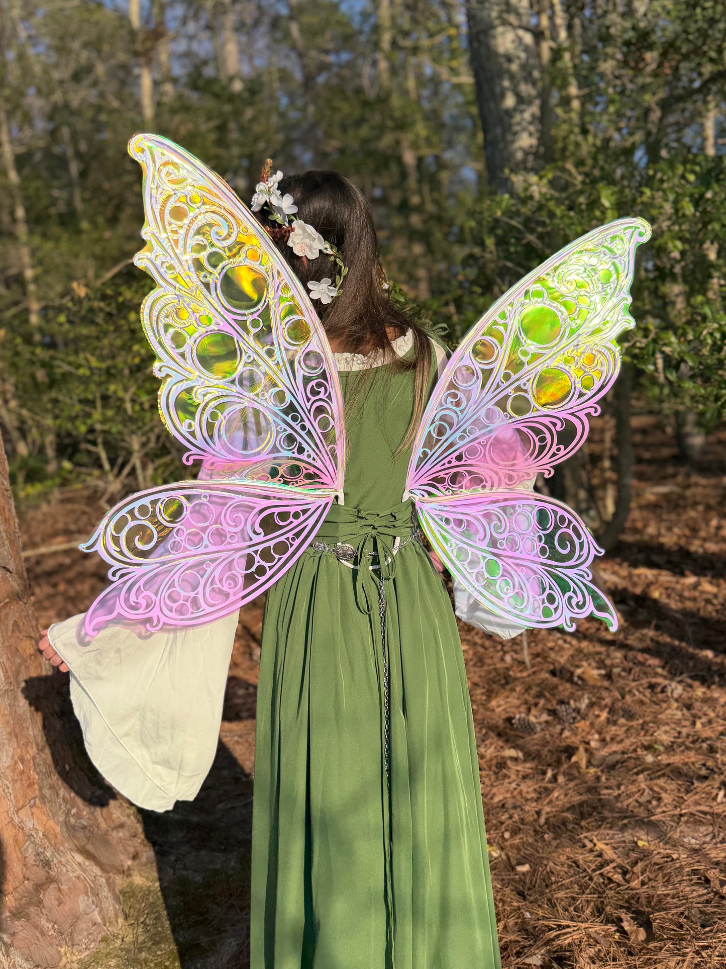 Person wearing a green dress with colorful fairy wings in a forest setting