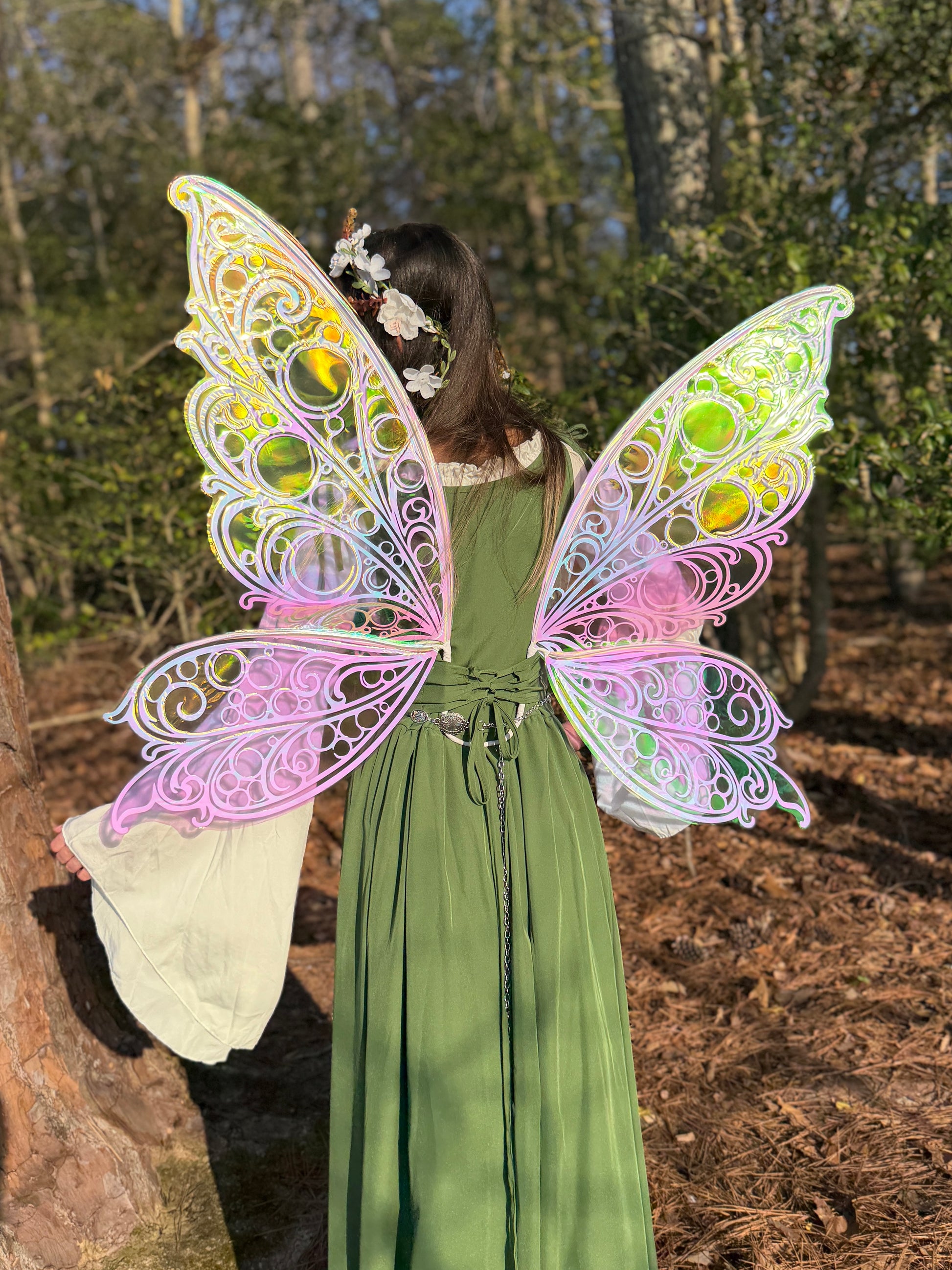 Person wearing a green dress with colorful fairy wings in a forest setting