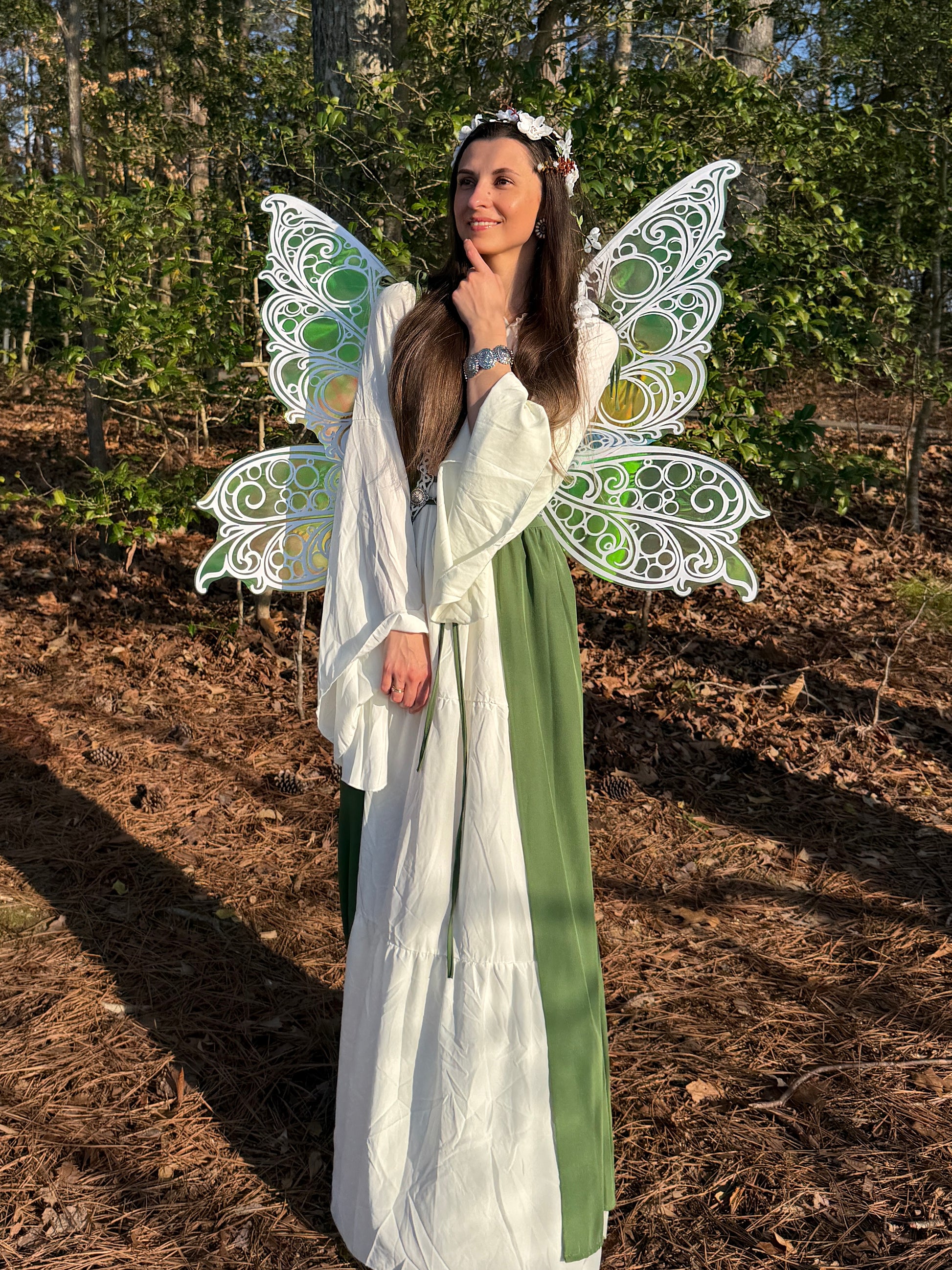Woman in a fairy costume with large, decorative wings standing in a forest setting.