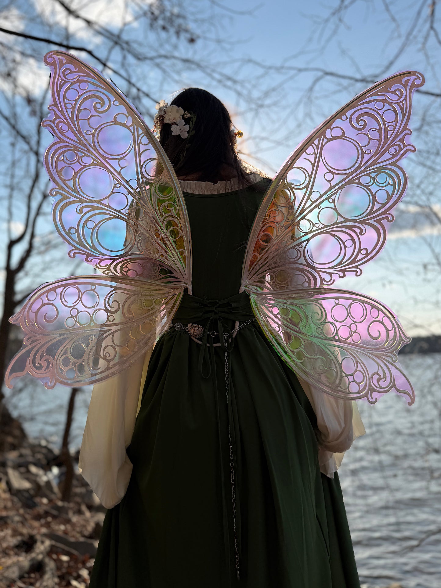 Person wearing iridescent fairy wings standing outdoors with a natural background