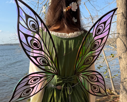 Person wearing green dress and large purple fairy wings standing by a body of water.
