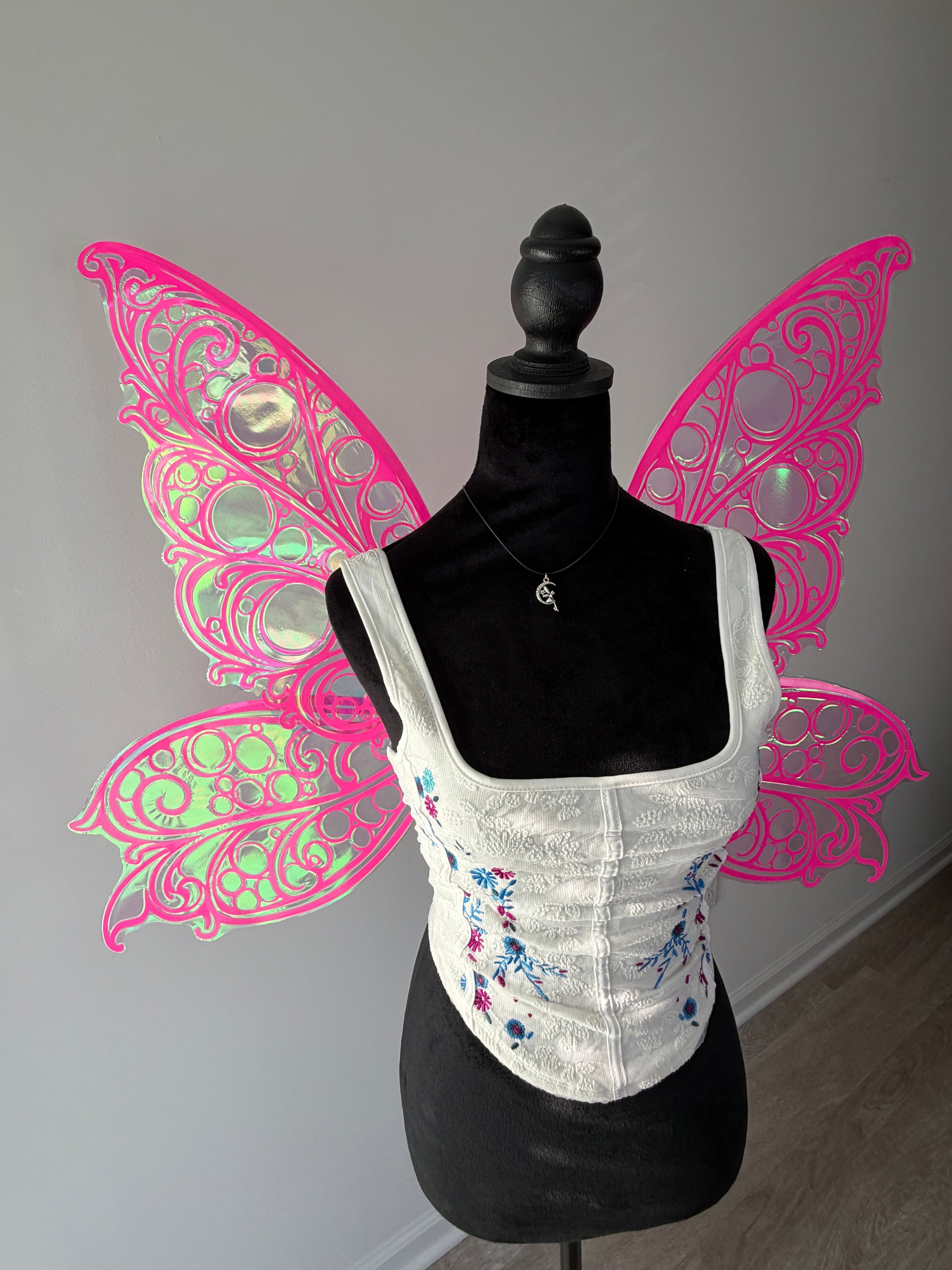 Mannequin wearing a white corset with pink butterfly wings on a gray background
